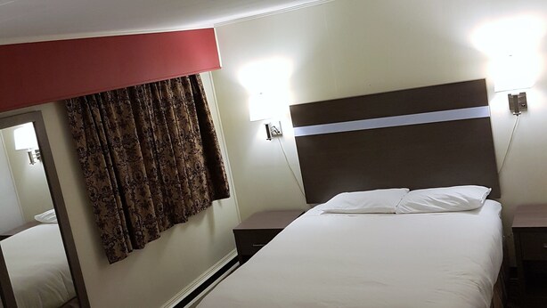A hotel room with two beds, a large mirror, a red accent wall, and a patterned curtain. - Holiday Motel & RV Resort (Hope)