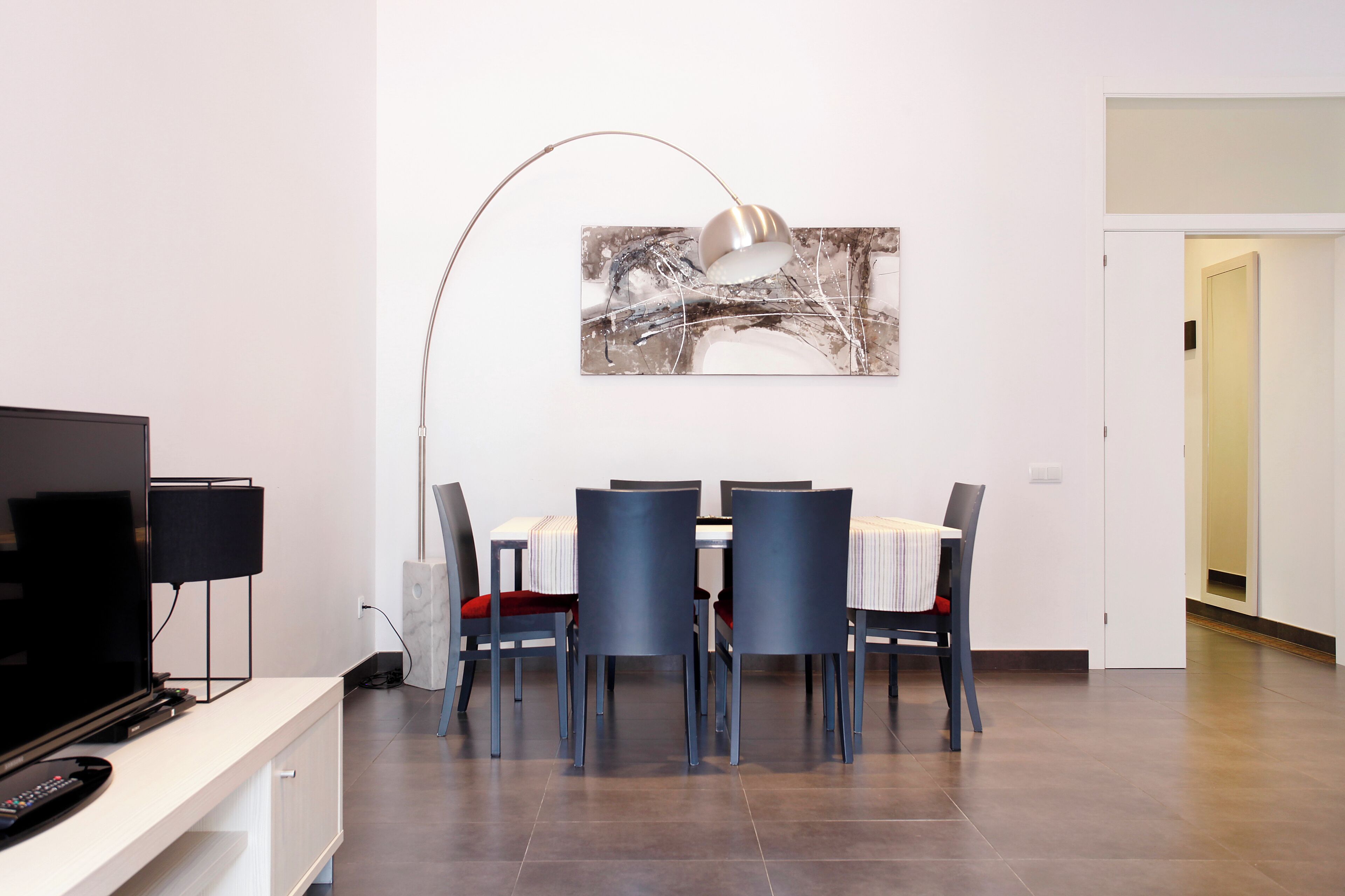A modern dining area with a table set for four, a television on a stand, and a floor lamp.