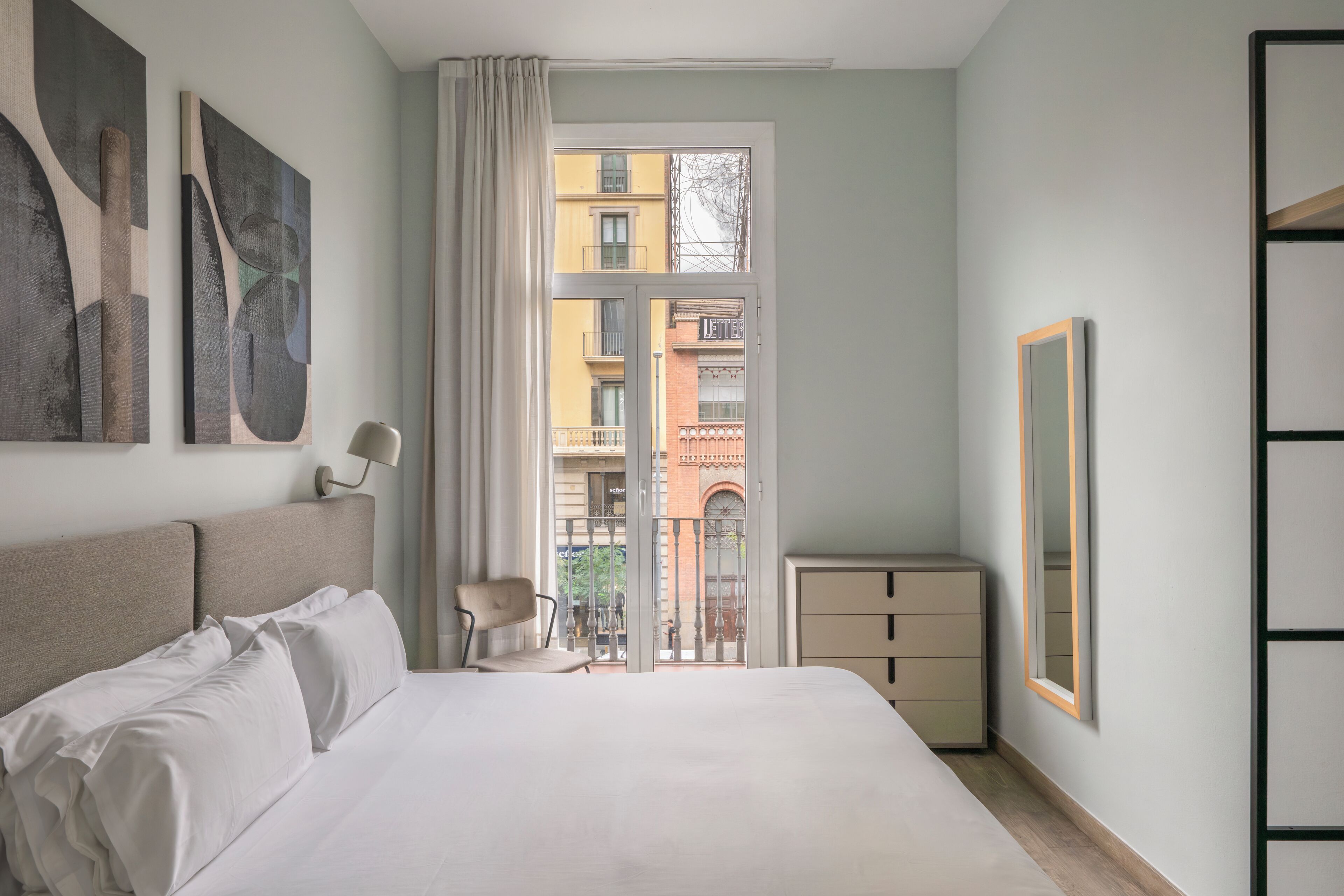 A bedroom with a large bed, a chair, a nightstand, and a window with a view of buildings.