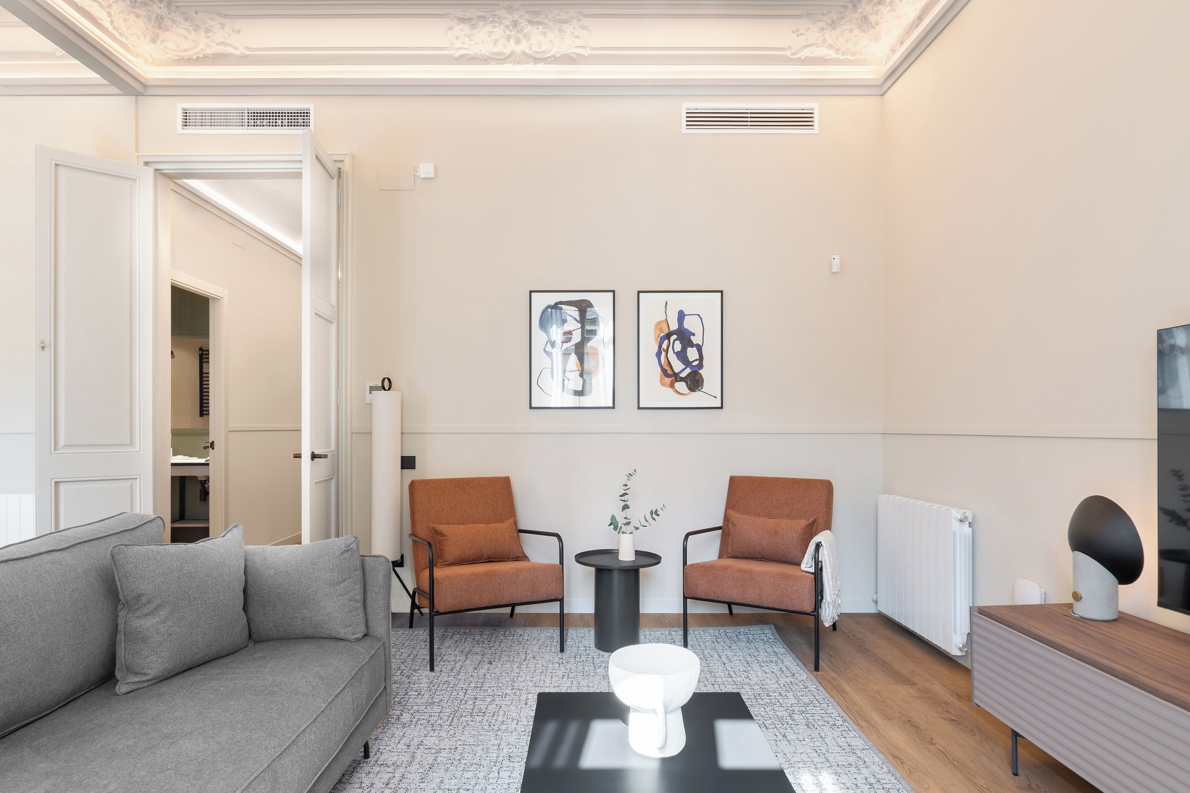 A modern living room with a grey sofa, two armchairs, a coffee table, and two framed artworks on the wall.
