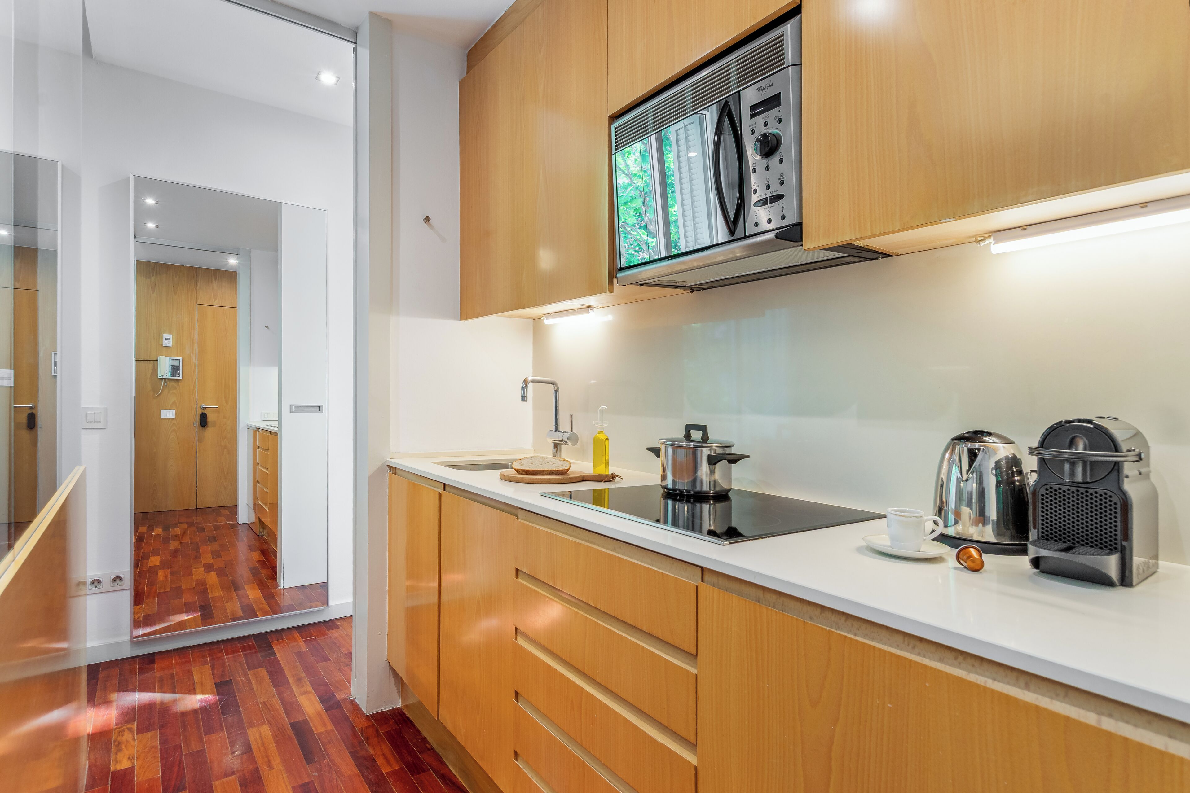 A modern kitchen with wooden cabinets, a microwave, a kettle, and a coffee maker.