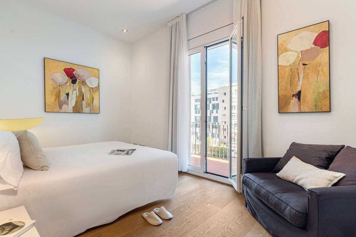 Una habitación de hotel moderna con una cama, un sofá de cuero oscuro y dos cuadros abstractos en las paredes.