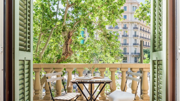 A balcony with a table and chairs, overlooking a tree and a building. - Aspasios Rambla Catalunya Suites  (Barcelona)