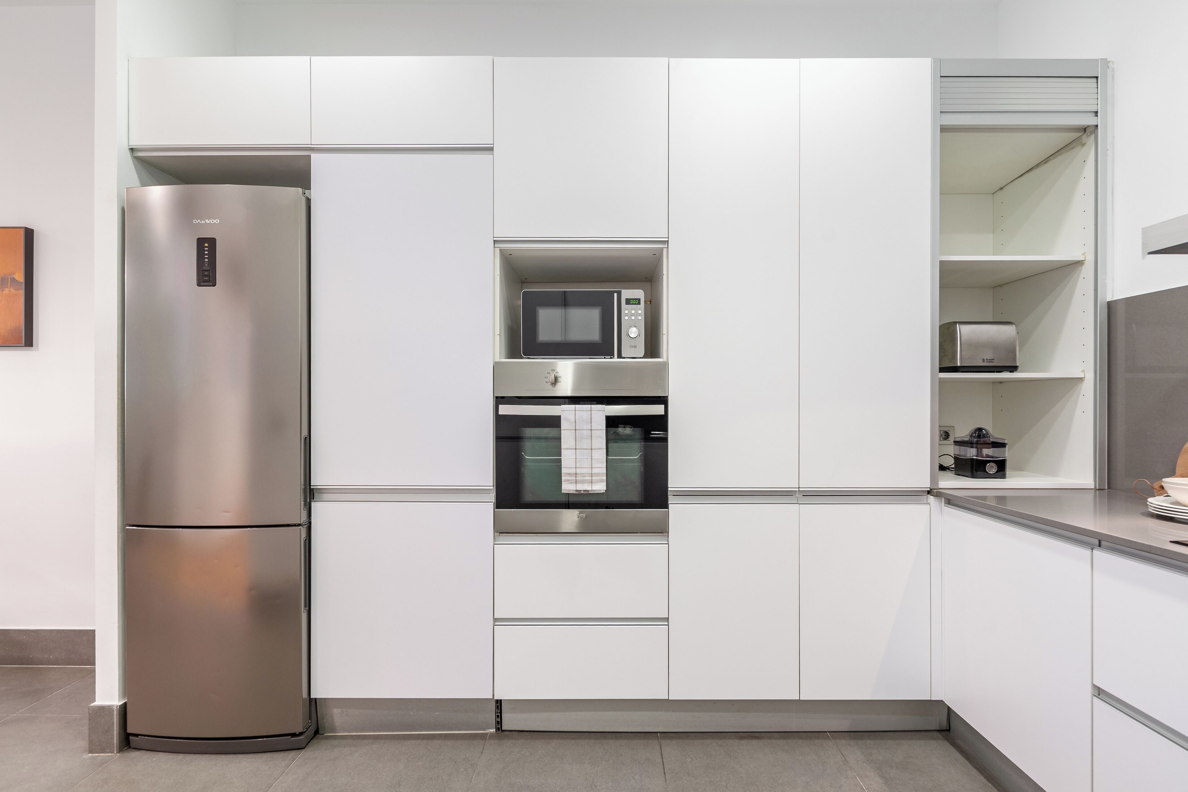 A modern kitchen with a built-in stainless steel refrigerator, microwave, oven, and a small pantry area.