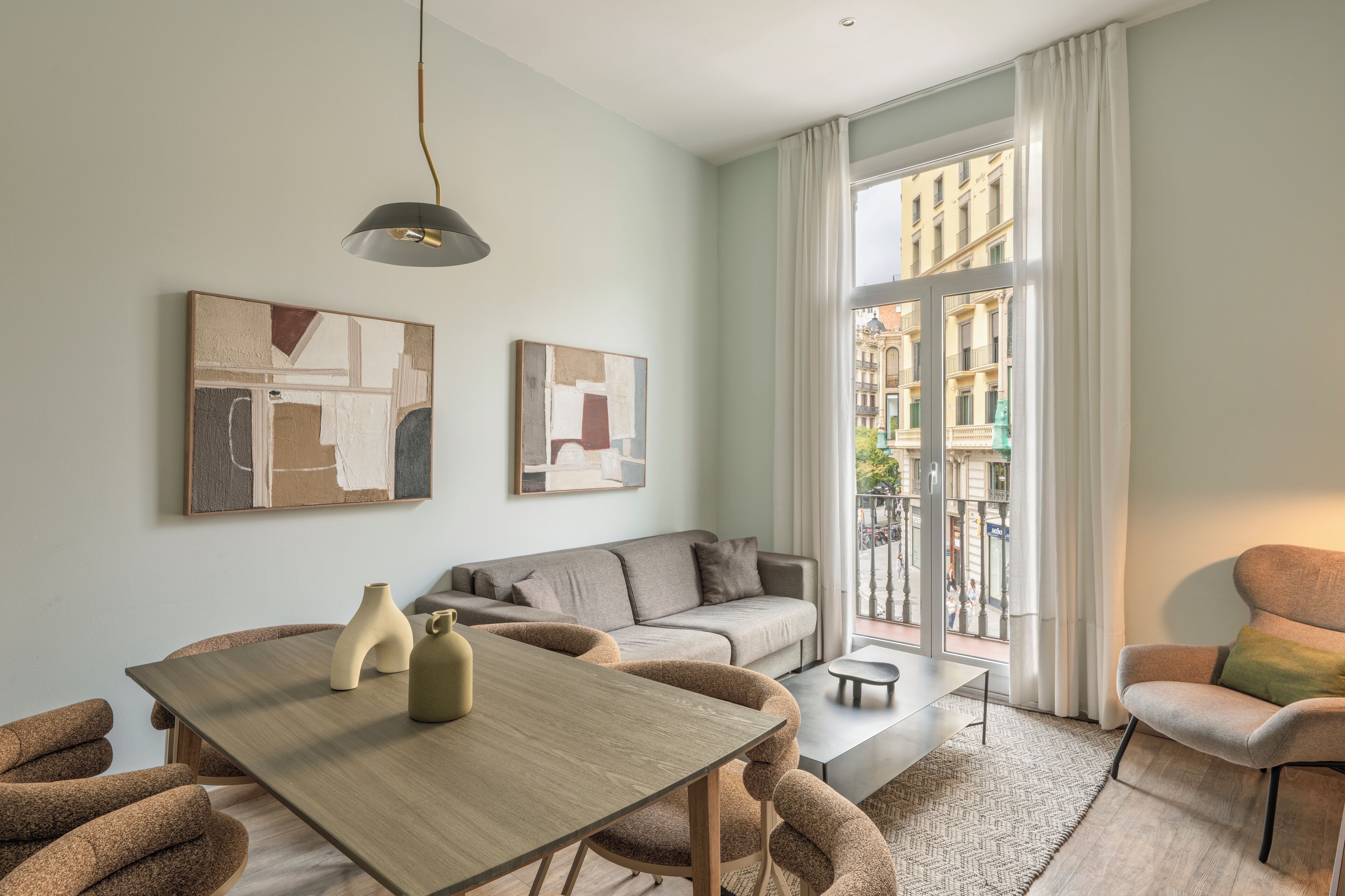 A modern living room with a sofa, a dining table with chairs, and artwork on the walls.