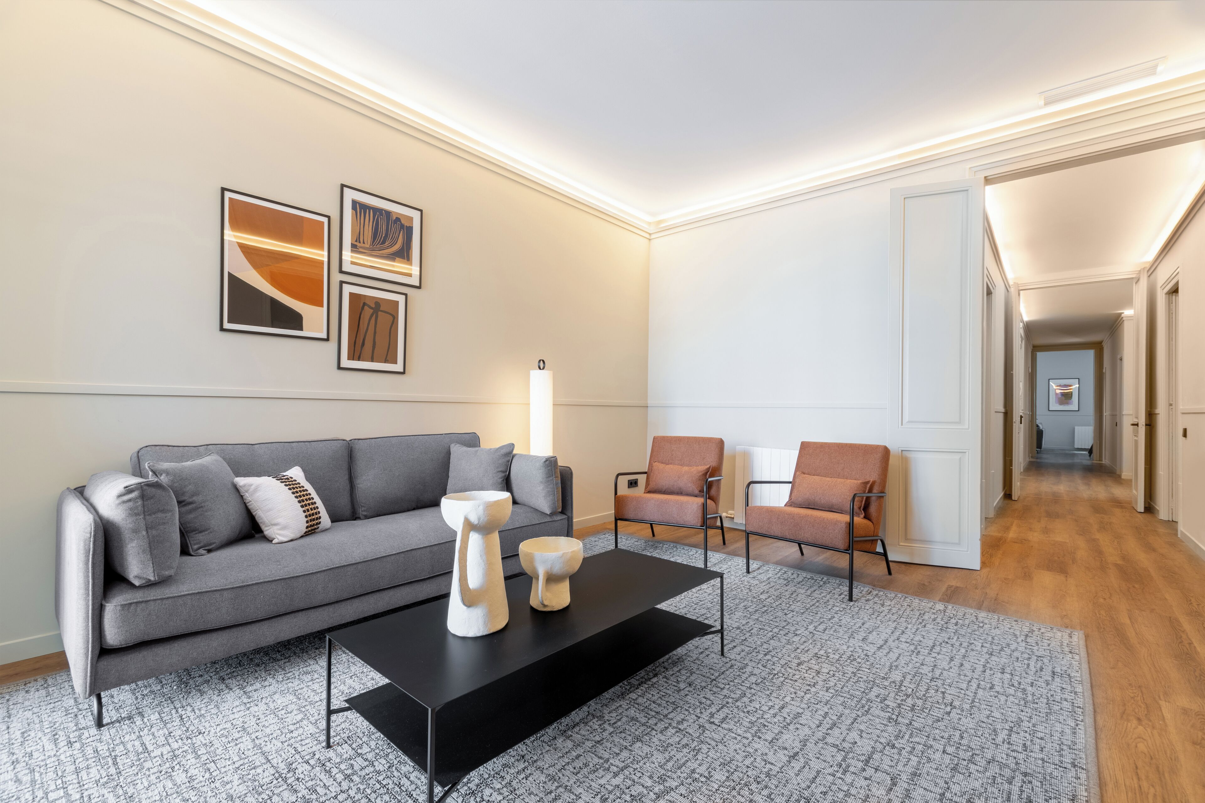 Ein modernes Wohnzimmer mit grauem Sofa, zwei Sesseln, einem schwarzen Couchtisch und abstrakten Wandbildern.