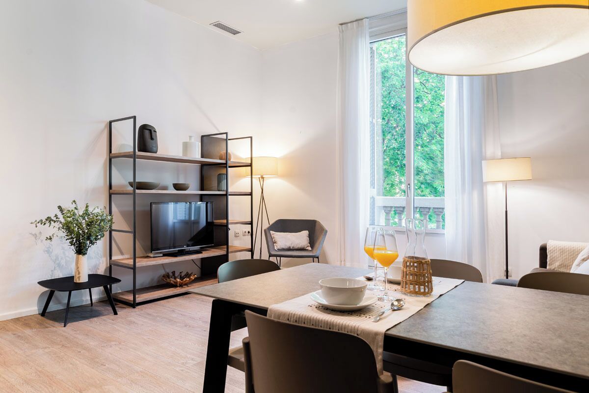 A modern living room with a TV, dining table, chairs, and a bookshelf.