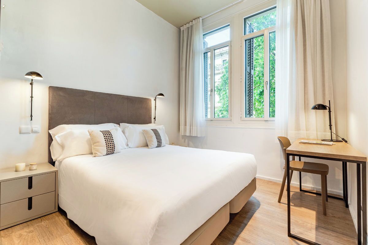 A neatly arranged bedroom with a large bed, bedside tables, a desk, and a chair.