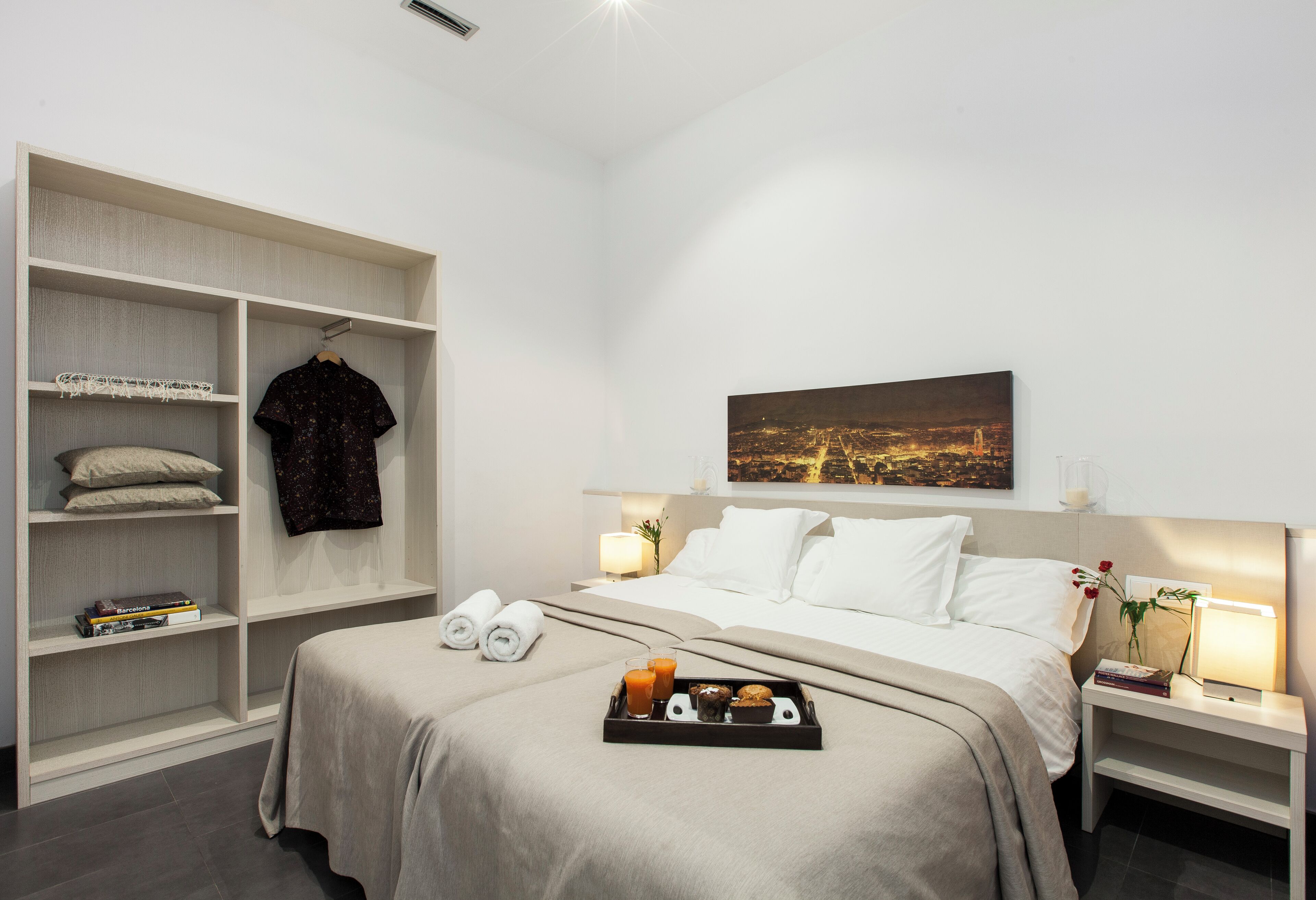 A modern hotel room with a neatly made bed, a large wardrobe, and a cityscape painting on the wall.