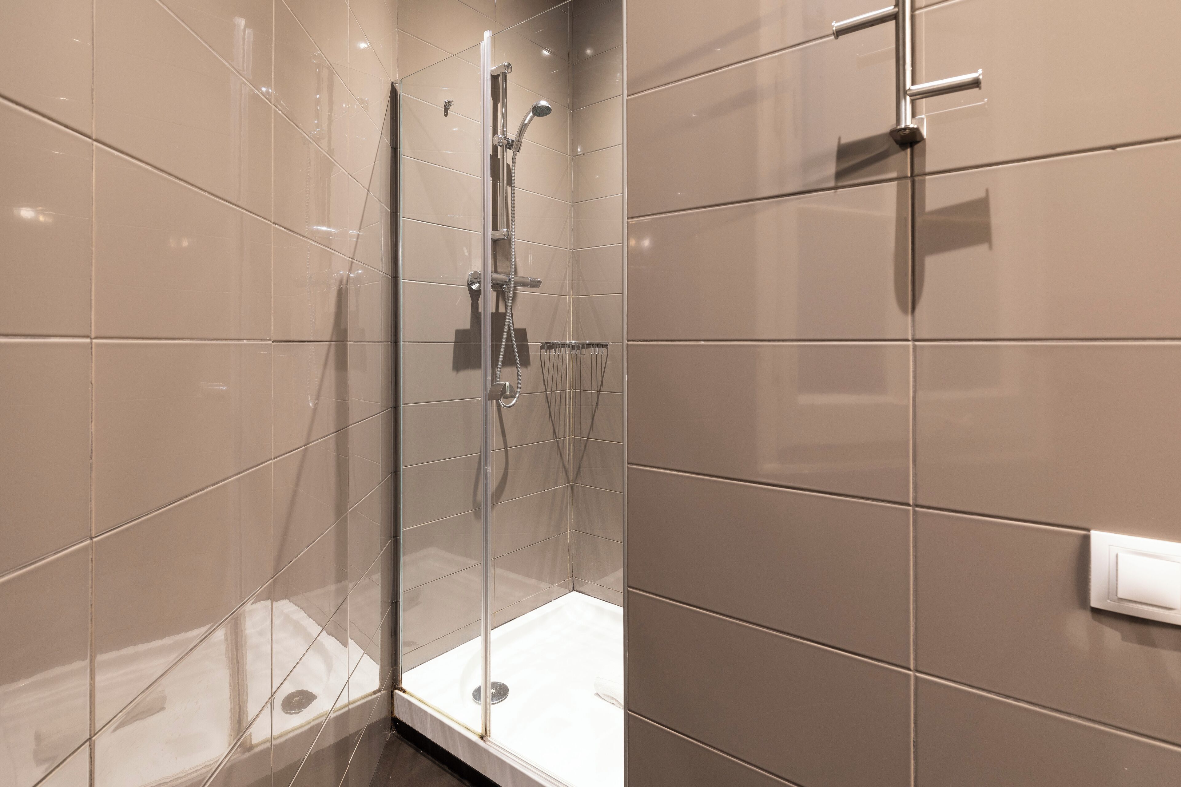 A modern bathroom with a glass shower enclosure, a white sink, and a wall-mounted faucet.