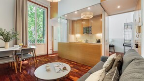A modern living room with a sofa, a dining table with chairs, a kitchen area, and a large window. - Aspasios Rambla Catalunya Suites  (Barcelona)