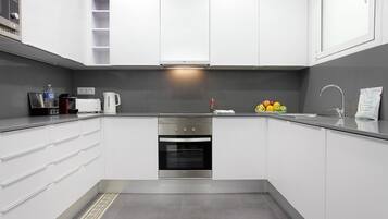 Een moderne keuken met witte kastjes, een ingebouwde oven, een rvs-afzuigkap en een grijze spatwand.