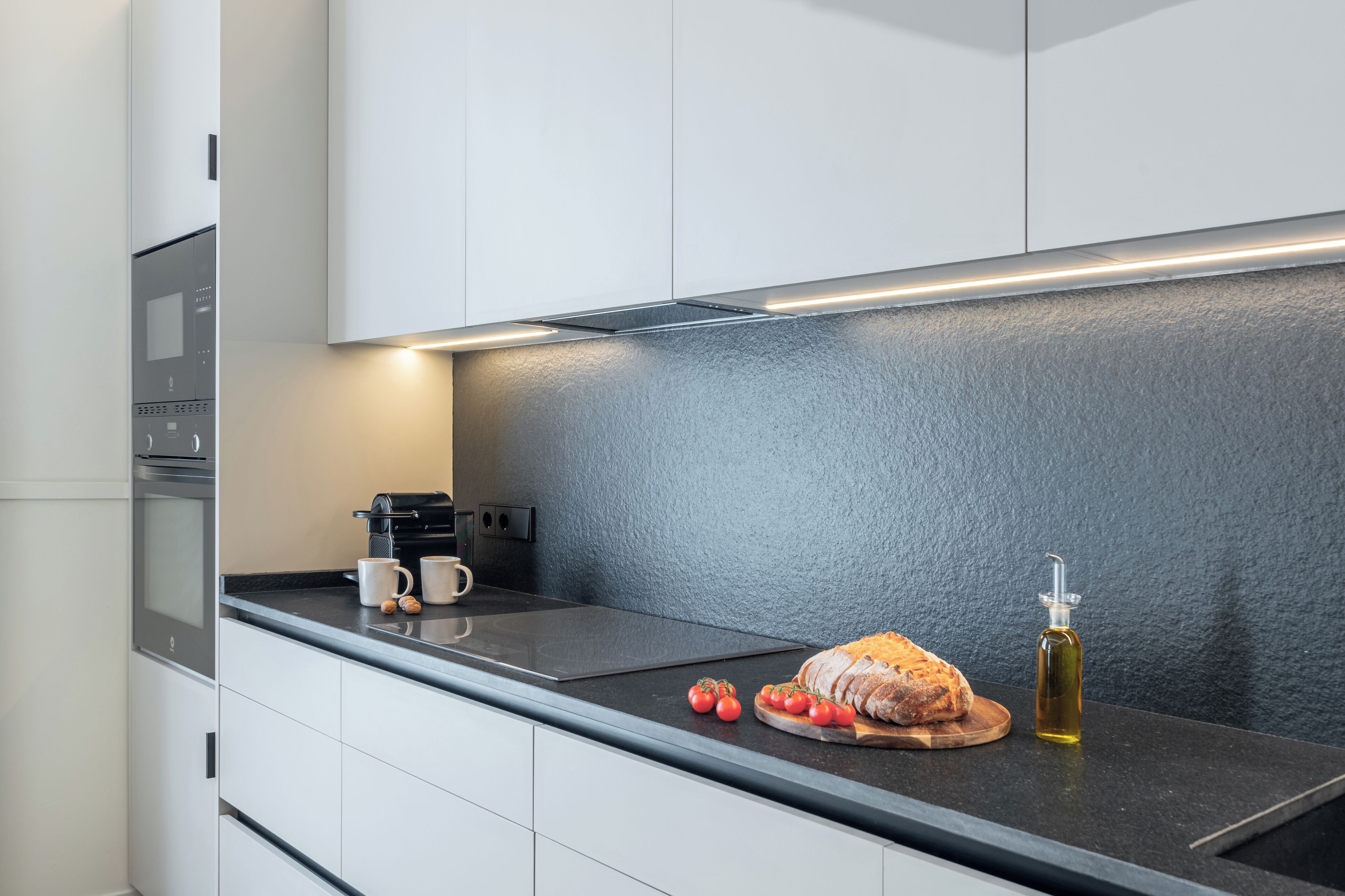 A modern kitchen with white cabinets, a black countertop, a built-in oven, and a coffee maker.
