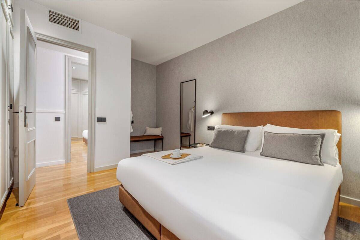 Una habitación de hotel moderna con una cama grande, una mesita de noche, un espejo y vistas al pasillo.