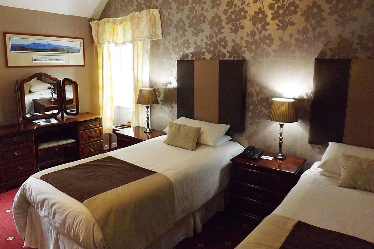 A hotel room with two beds, a desk, a dresser, and a mirror.