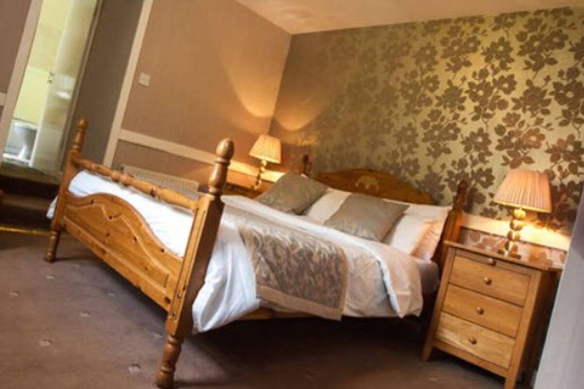 A bedroom with a wooden bed, a nightstand, a lamp, and floral wallpaper.