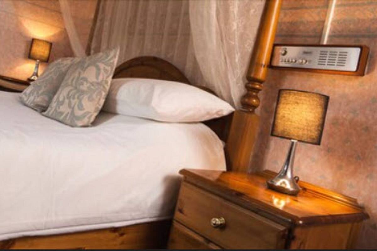 A neatly made bed with white linens, a wooden headboard, and a bedside lamp.