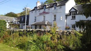A traditional Stagecoach Inn building with a stone wall in front, surrounded by greenery. - Cairndow Stagecoach Inn (Cairndow)