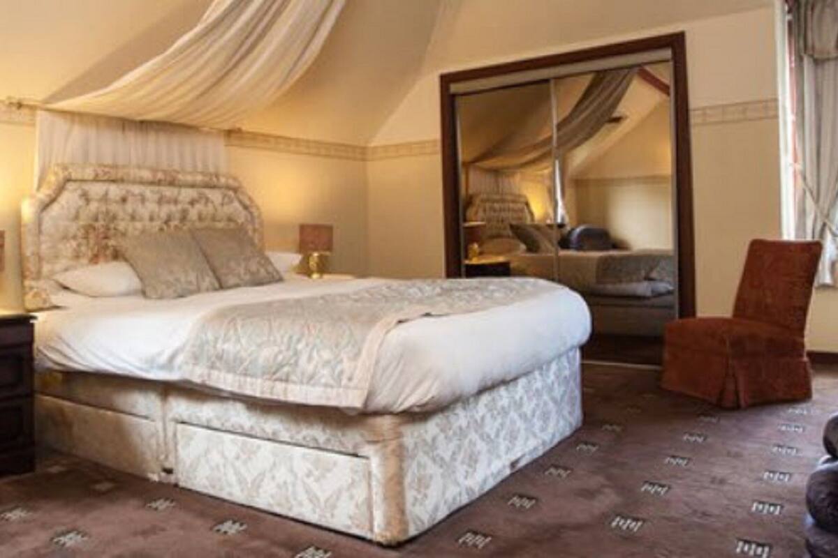 A spacious bedroom with a large bed, a nightstand, a chair, and a mirror.