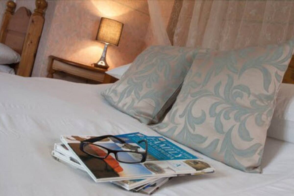 A neatly made bed with a pillow and a magazine with glasses on it.