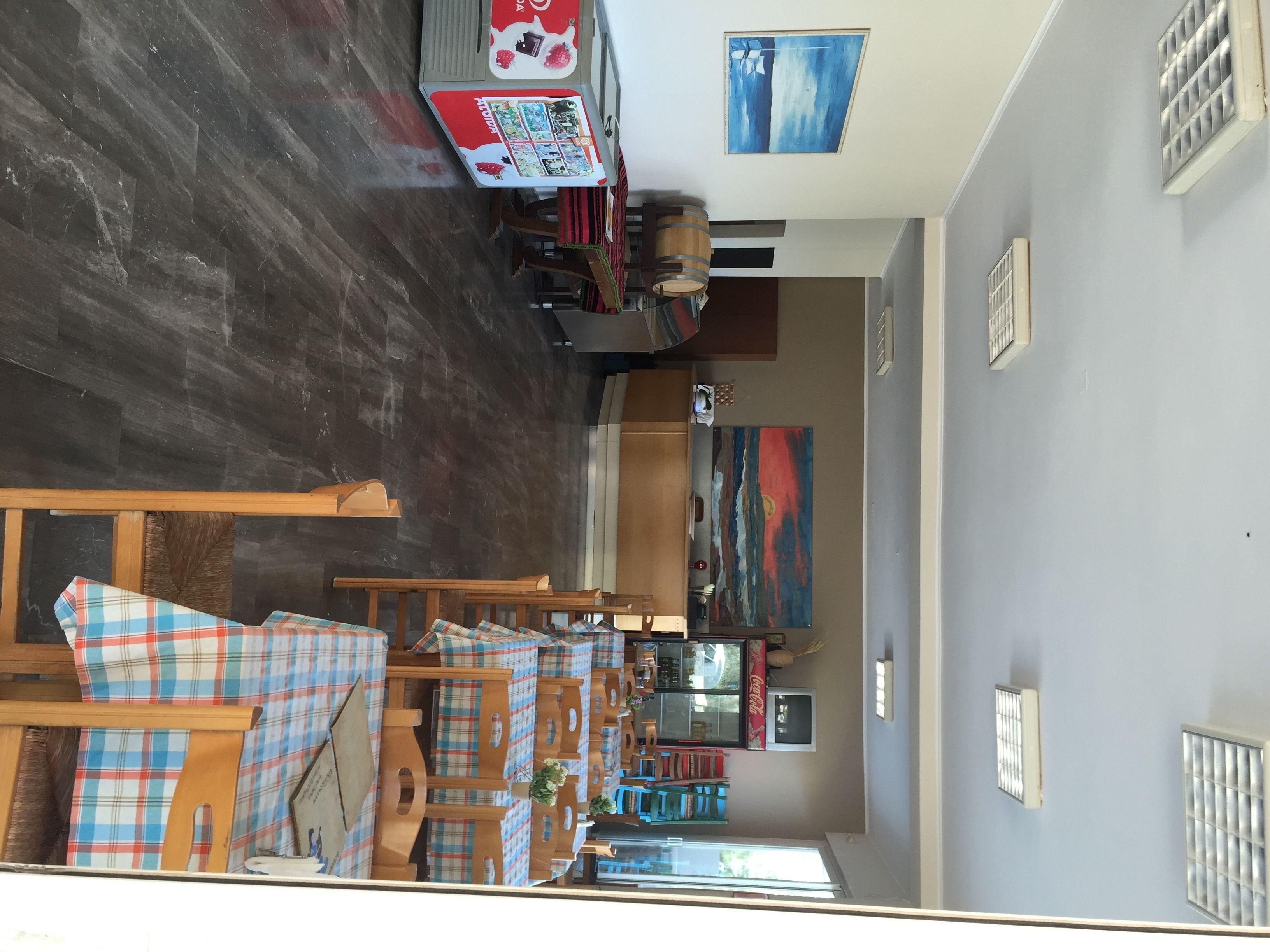 A room with a dark wooden floor, a dining area with plaid-covered chairs, a table with a Coca-Cola sign, and a colorful abstract painting on the wall.