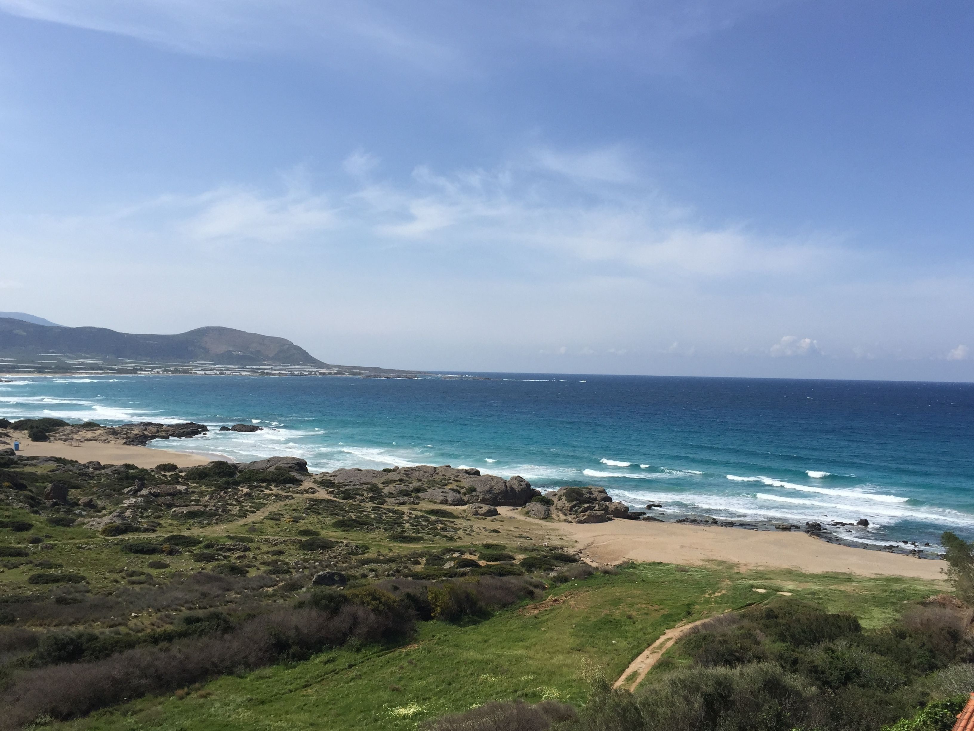 A coastal landscape with a beach, rocky terrain, and distant mountains.