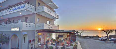A hotel with a reception area, outdoor seating, and a view of the sunset over the water.