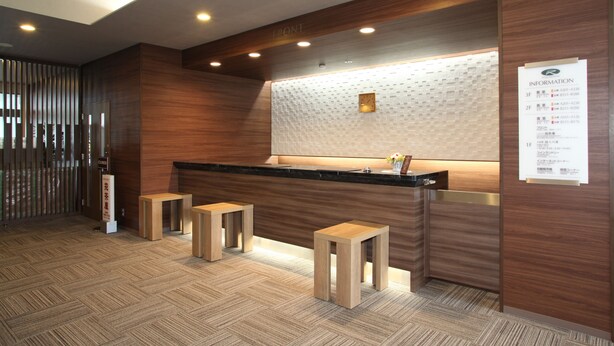 A reception area with a wooden reception desk, two wooden stools, a wall clock, and a signboard with information. - HOTEL ROUTE-INN Kesennuma ChuoInter (Kesennuma)