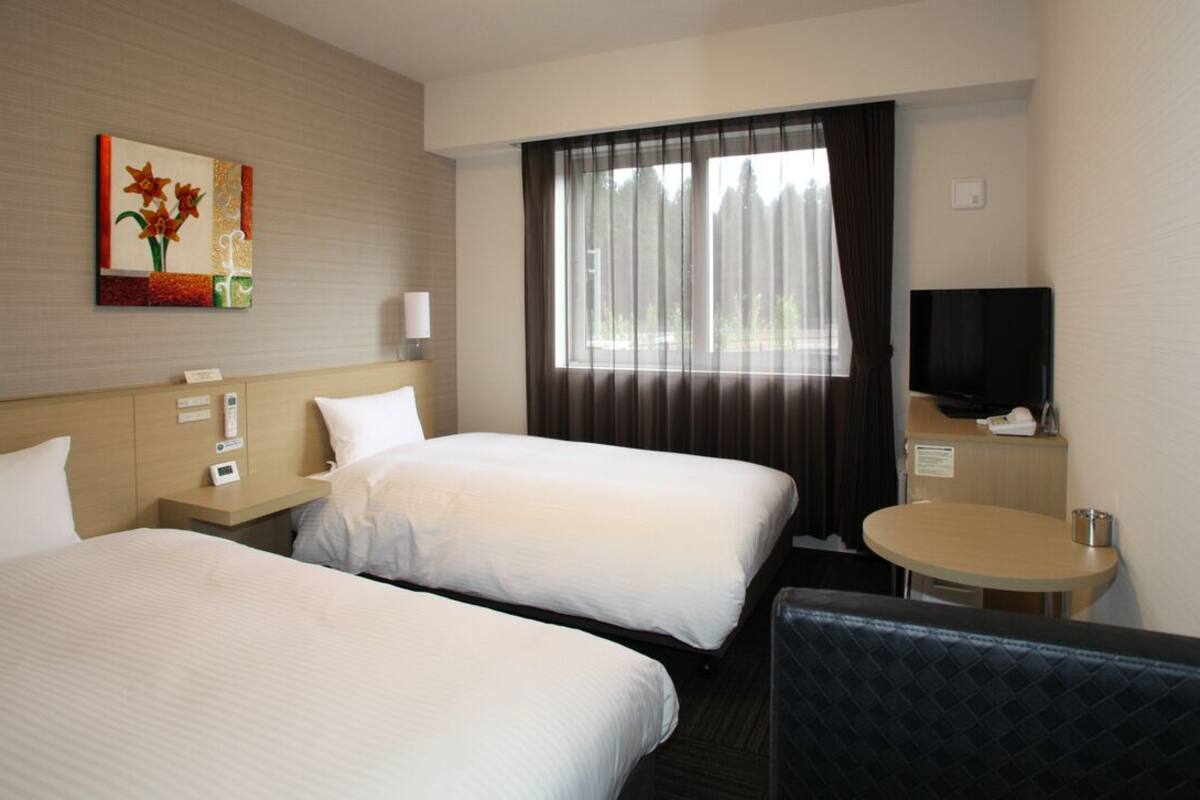 A hotel room with two beds, a television, a small table, and a painting on the wall.