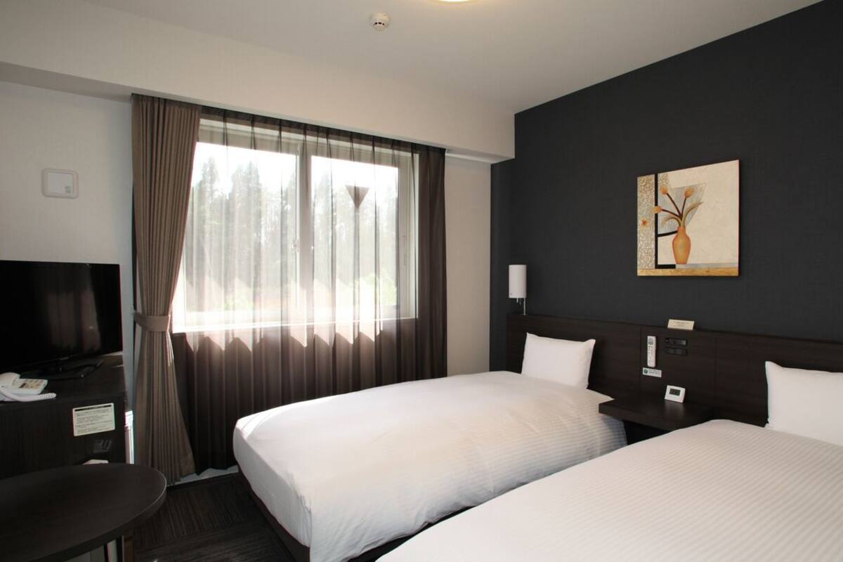 A hotel room with two beds, a desk, a television, and a painting on the wall.