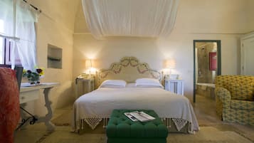 Quarto com cama grande, duas mesas de cabeceira com abajures, um banquinho verde, uma cadeira e uma janela com cortinas.