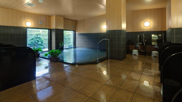 Een modern binnenzwembad met houten plafond en betegelde vloer, omringd door zwarte zitplaatsen en potplanten.
