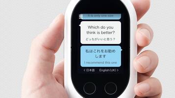 A hand holding a white pocket-sized device with a screen displaying text in English and Japanese.