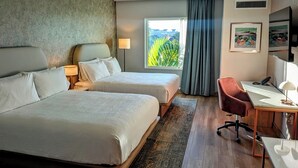 A hotel room with two beds, a desk, a chair, a window with curtains, and a framed picture on the wall. - Sea Glass Beach Place, Trademark Collection by Wyndham (Lauderdale-by-the-Sea)