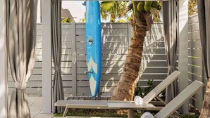 A poolside area with lounge chairs, a surfboard, and a palm tree. - Sea Glass Beach Place, Trademark Collection by Wyndham (Lauderdale-by-the-Sea)