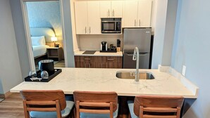 A modern kitchen with a large island, wooden chairs, and white cabinets. - Sea Glass Beach Place, Trademark Collection by Wyndham (Lauderdale-by-the-Sea)