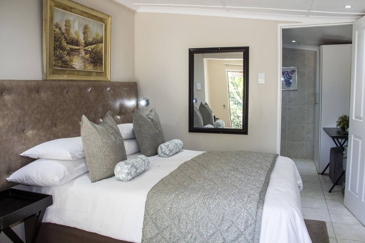 A neatly arranged bedroom with a large bed, a headboard, and a mirror.