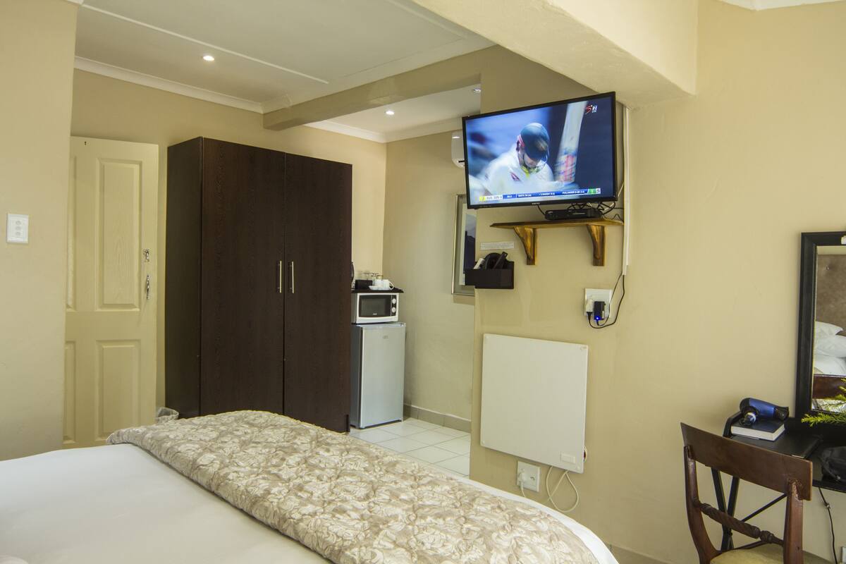 A hotel room with a bed, a TV mounted on the wall, a microwave, a small desk with a chair, and a wardrobe.