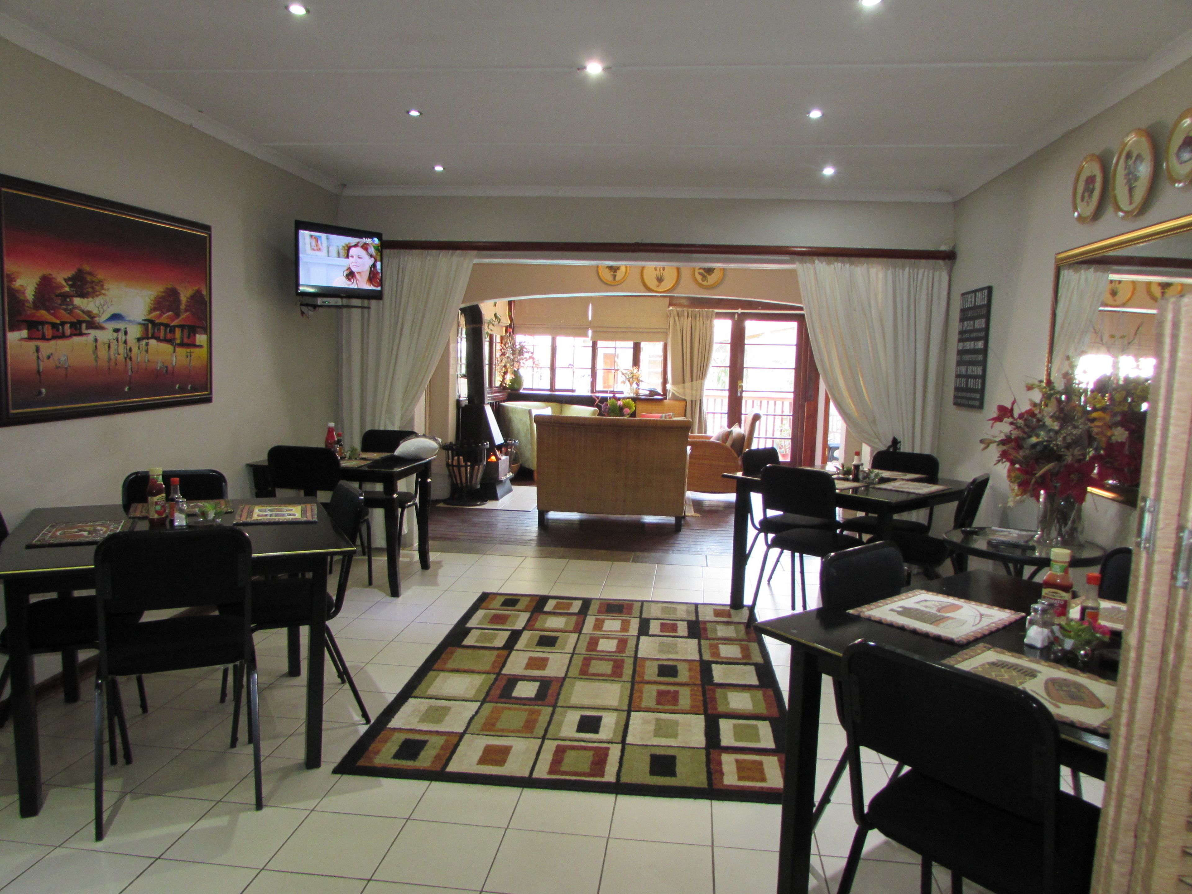 Un comedor de hotel con televisión, mesas, sillas, un tapete estampado y vistas a la cocina y la zona de bar.