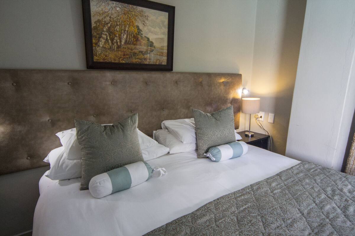 A neatly made bed with a tufted headboard, white and grey pillows, and a patterned bedspread.