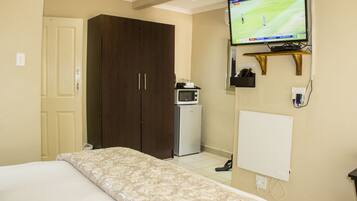 A hotel room with a bed, a wardrobe, a television mounted on the wall, a small refrigerator, and a power outlet.