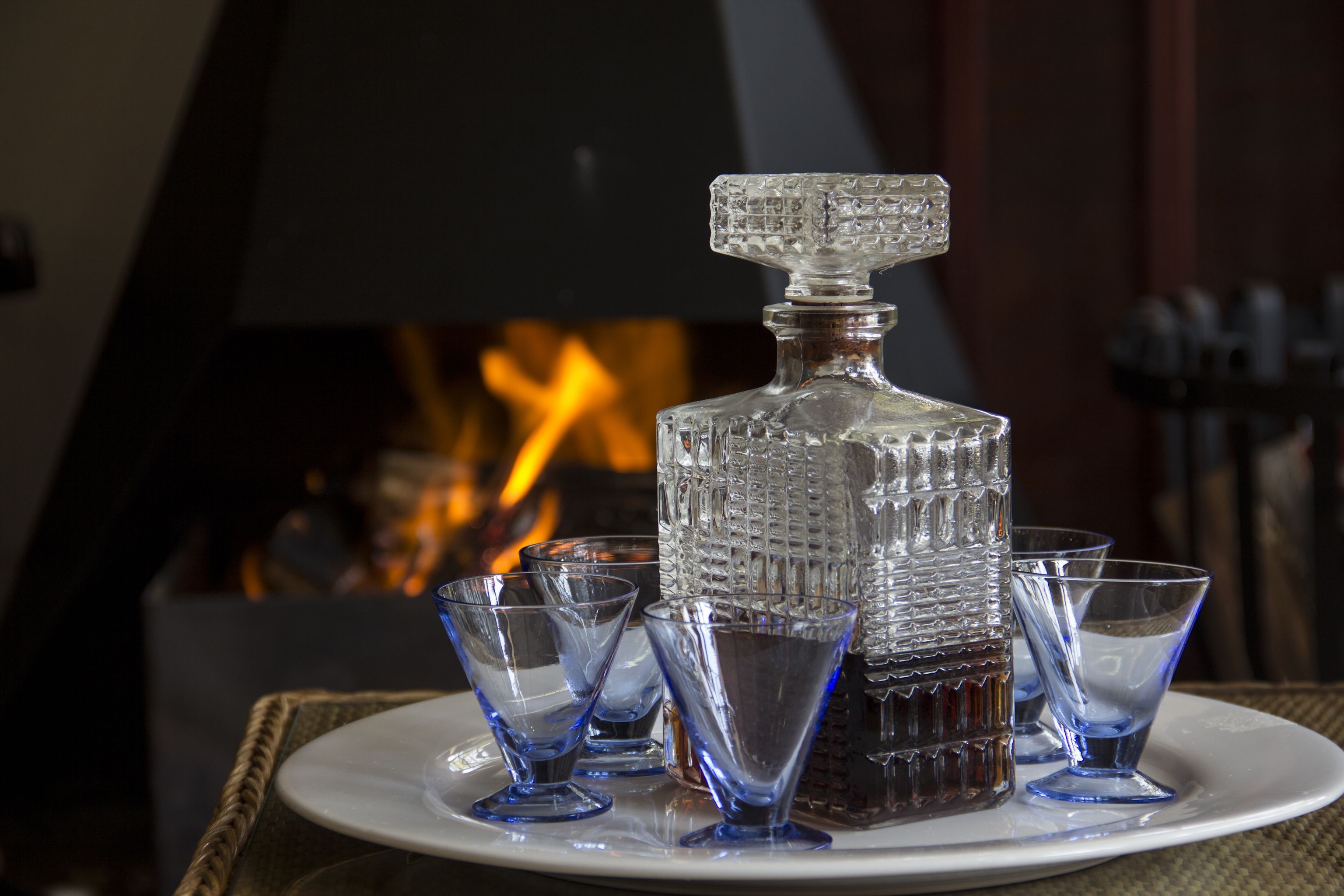 A crystal decanter and several glasses on a white plate, set against a backdrop of a fireplace.