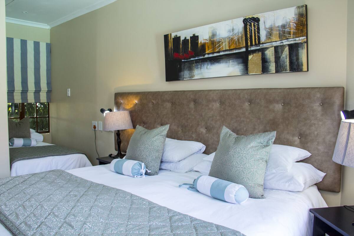 A hotel room with two beds, a large painting on the wall, and a window with blinds.
