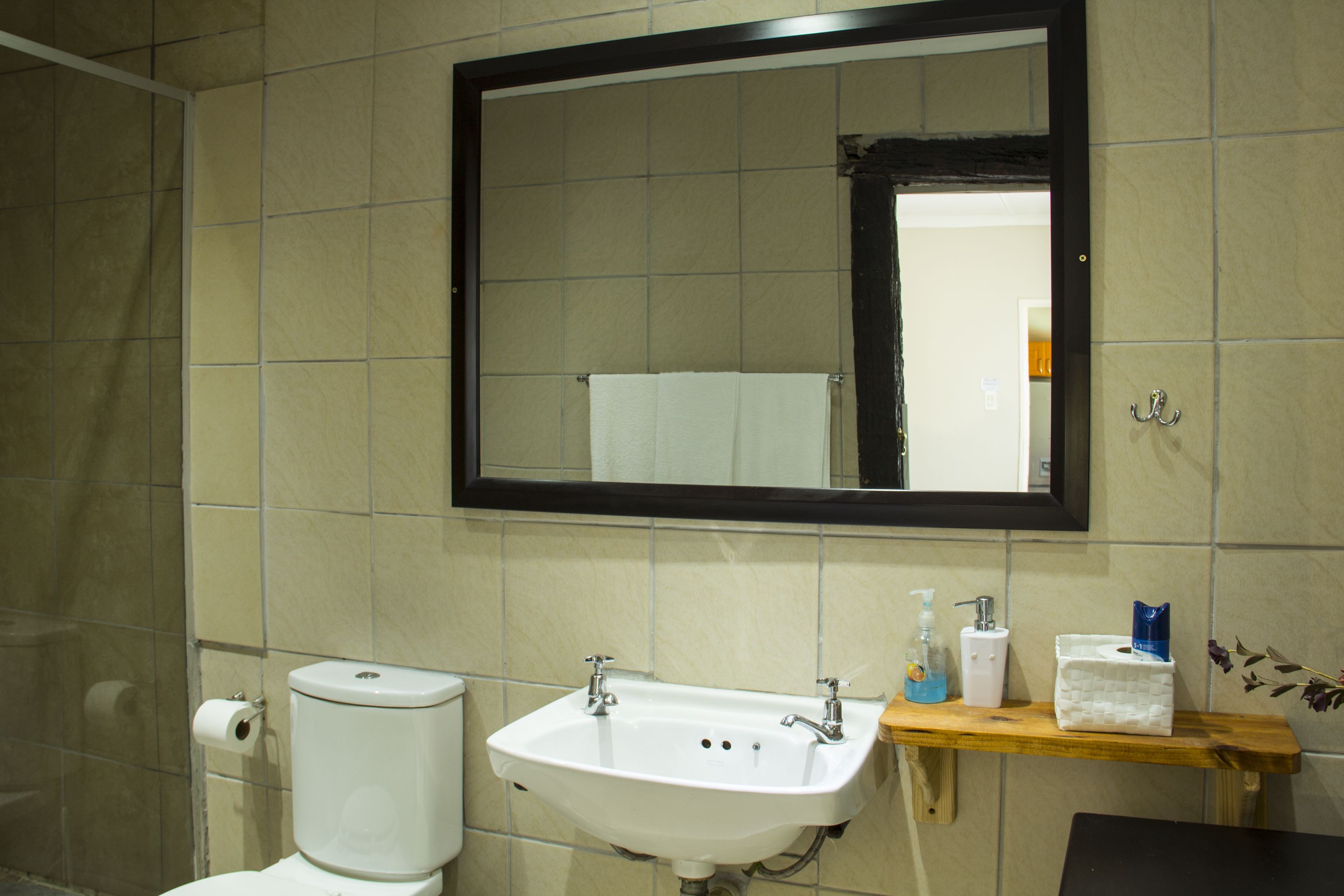 A bathroom with a white sink, a mirror, and a wooden shelf with toiletries.