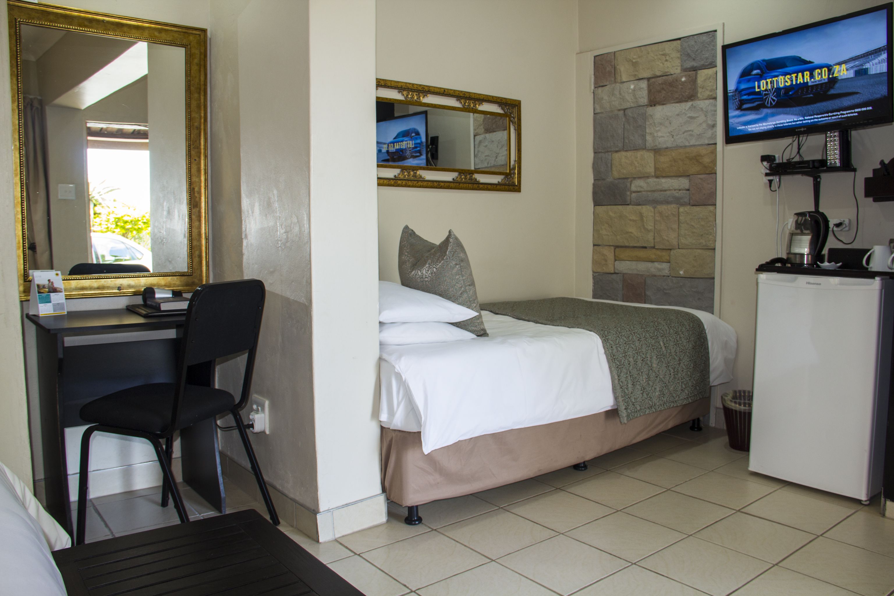 A hotel room with a bed, a desk with a chair, a television mounted on the wall, and a refrigerator.