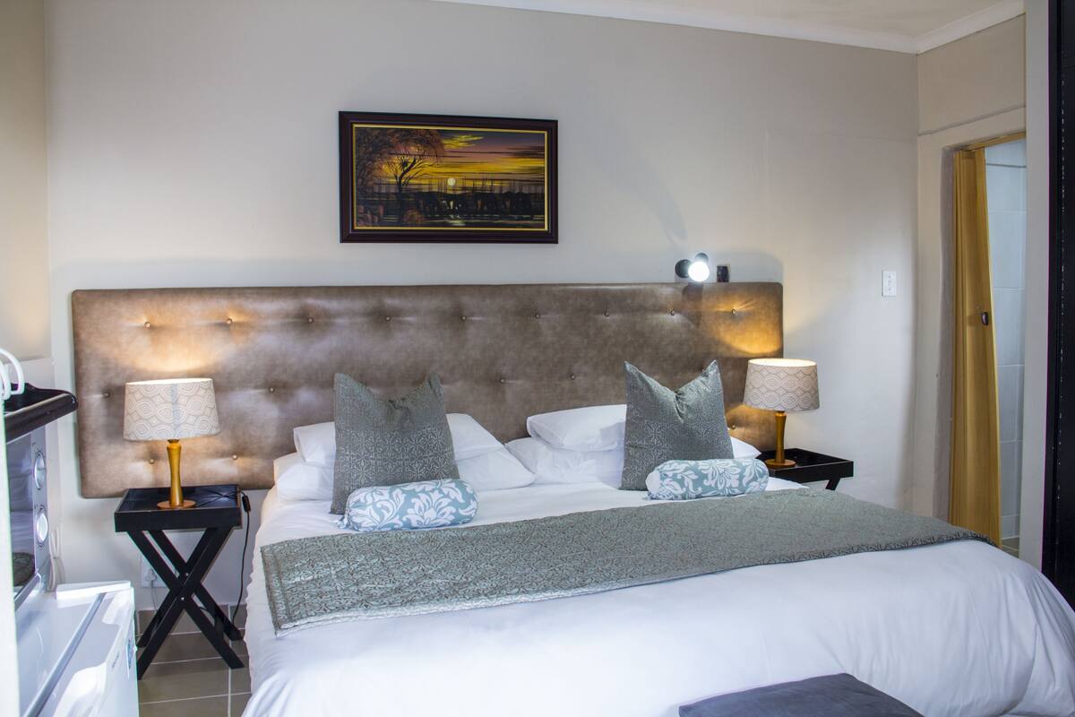 A neatly made bed with a tufted headboard, two bedside tables with lamps, and a framed picture on the wall.
