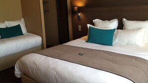 Une chambre d’hôtel avec deux lits, chacun doté de draps blancs et d’oreillers turquoise. On y trouve une tête de lit en bois et un luminaire fixé au mur.