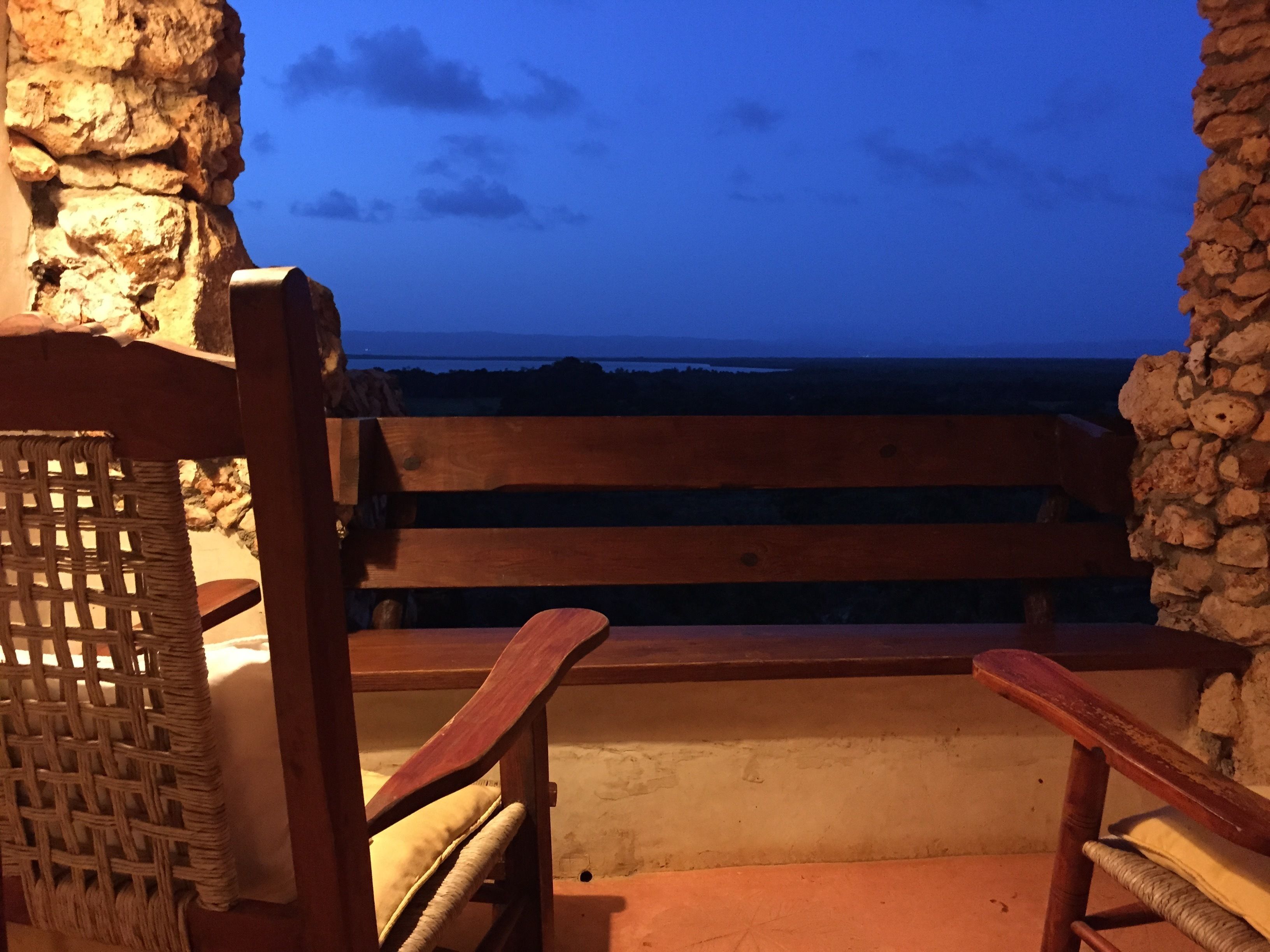 Un banc en bois doté d’un dossier en osier, placé devant un mur de pierre, et d’où l’on peut admirer un plan d’eau au crépuscule.