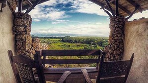 Un banco de madera rústica con pilares de piedra, con vistas a un paisaje verde exuberante bajo un cielo despejado.