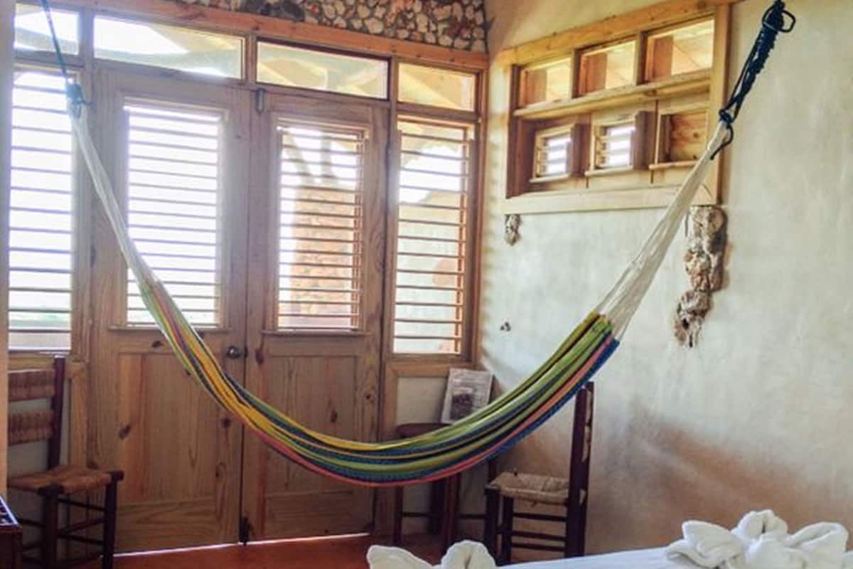 A room with a bed, a hammock, wooden doors, and a stone wall.